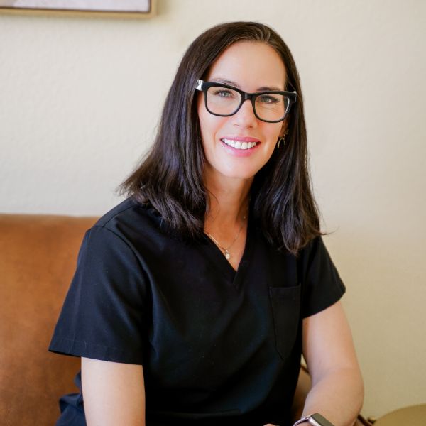 Smiling woman with glasses sitting on a brown couch.
