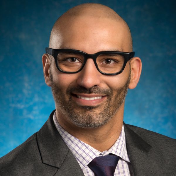 A professional man in glasses and a suit smiling.