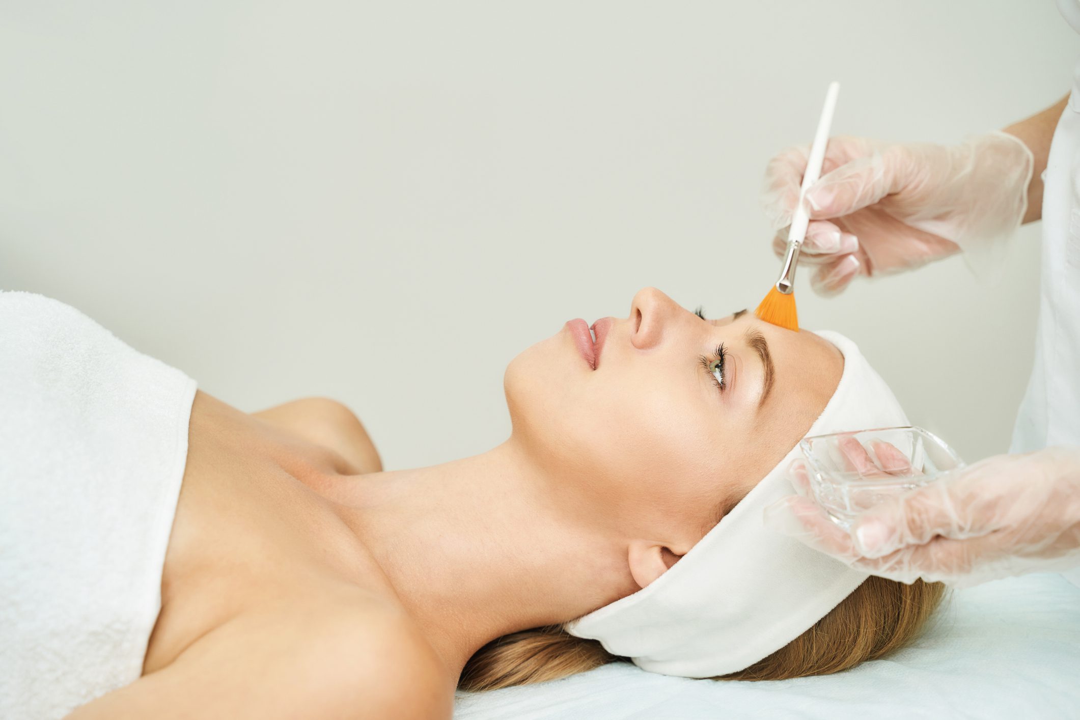 Woman receiving facial treatment with a brush at a spa.