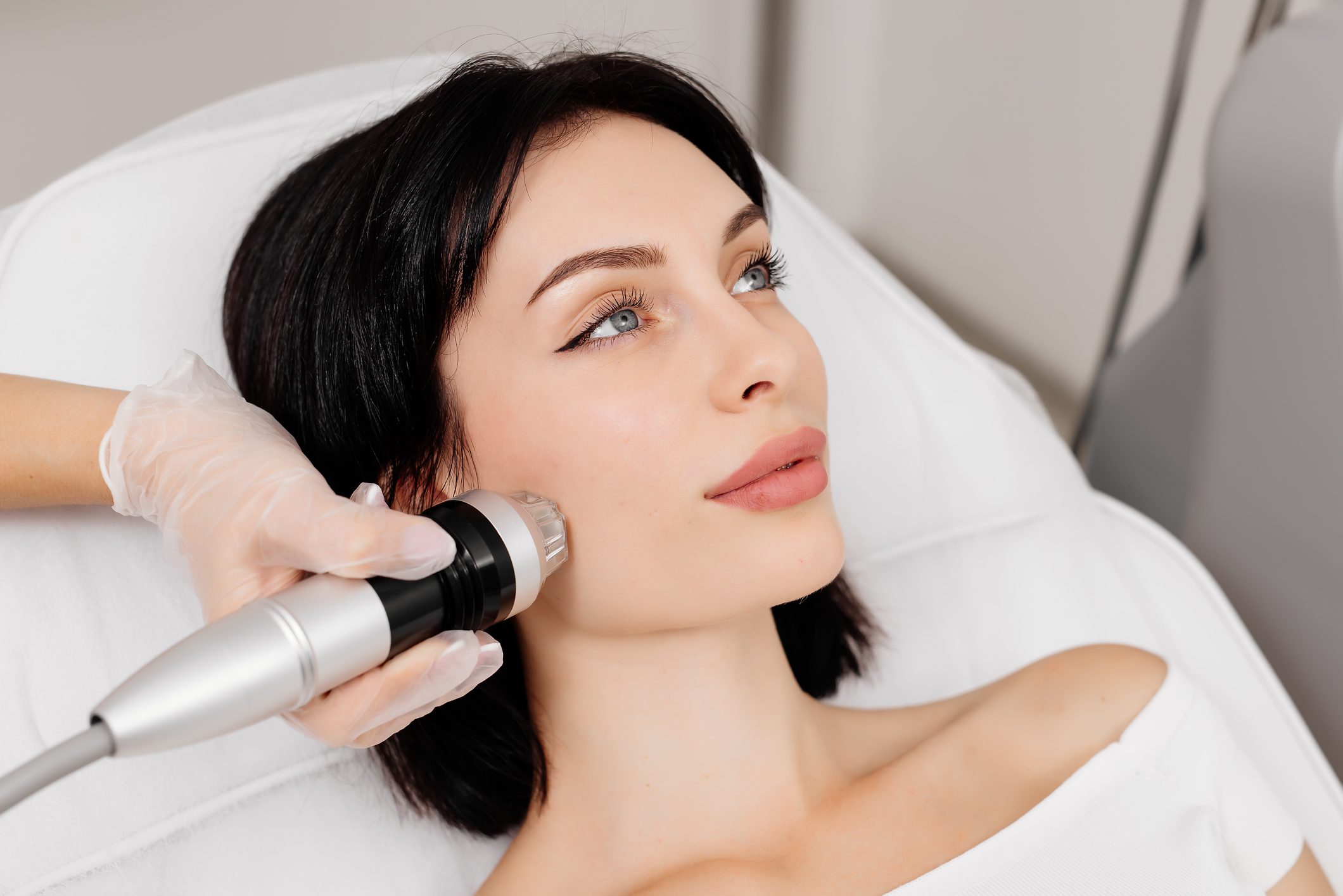 Woman receiving a facial treatment with a handheld device.