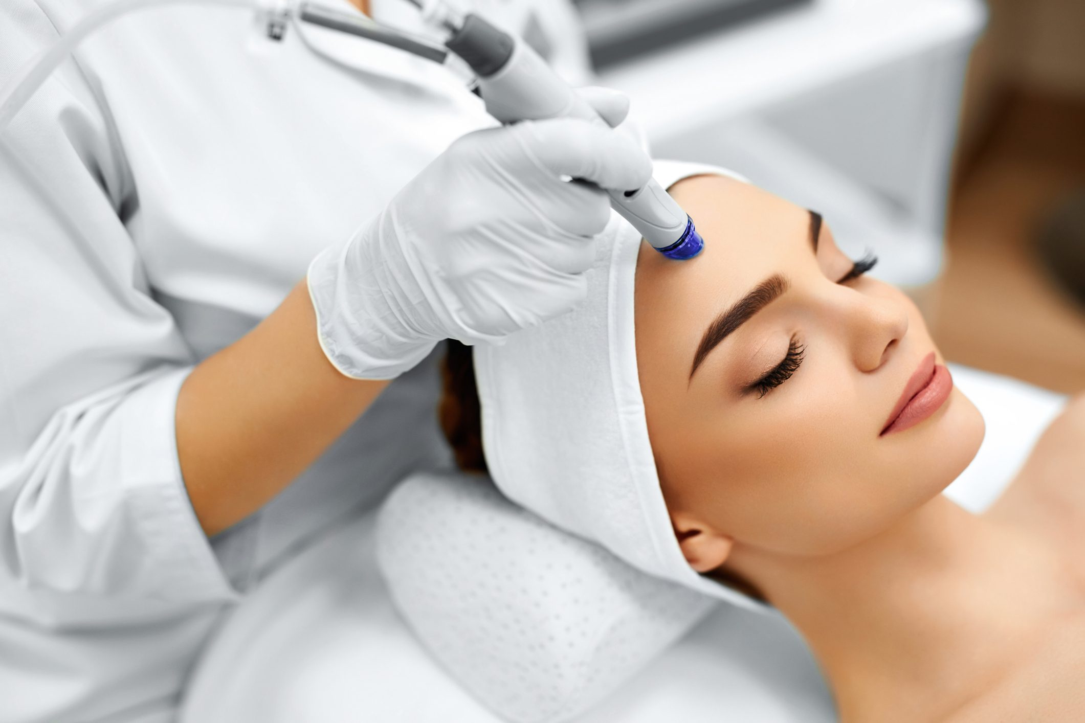A woman receiving a facial treatment with a modern skincare device.