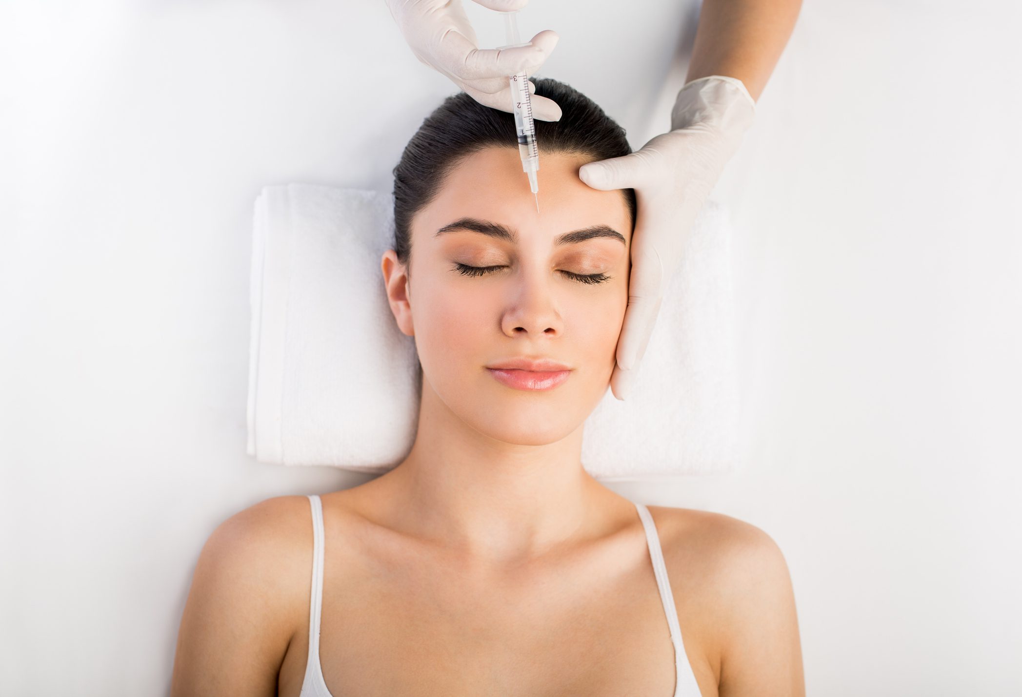A woman receiving a skincare treatment with a white cream applied to her forehead.