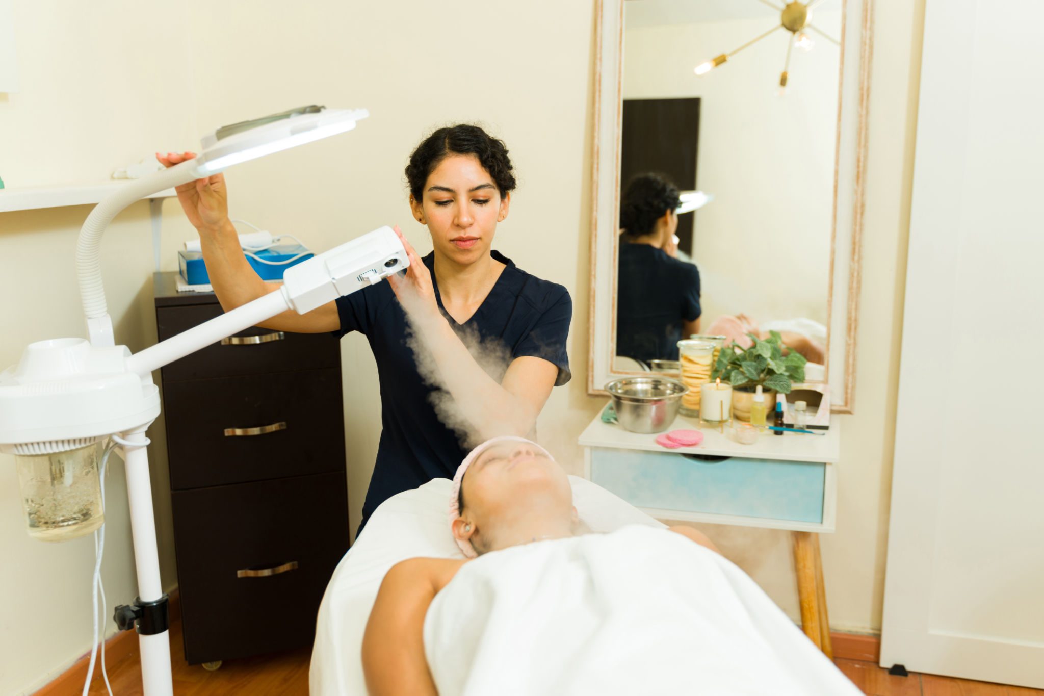 Woman providing facial treatment with steam machine.