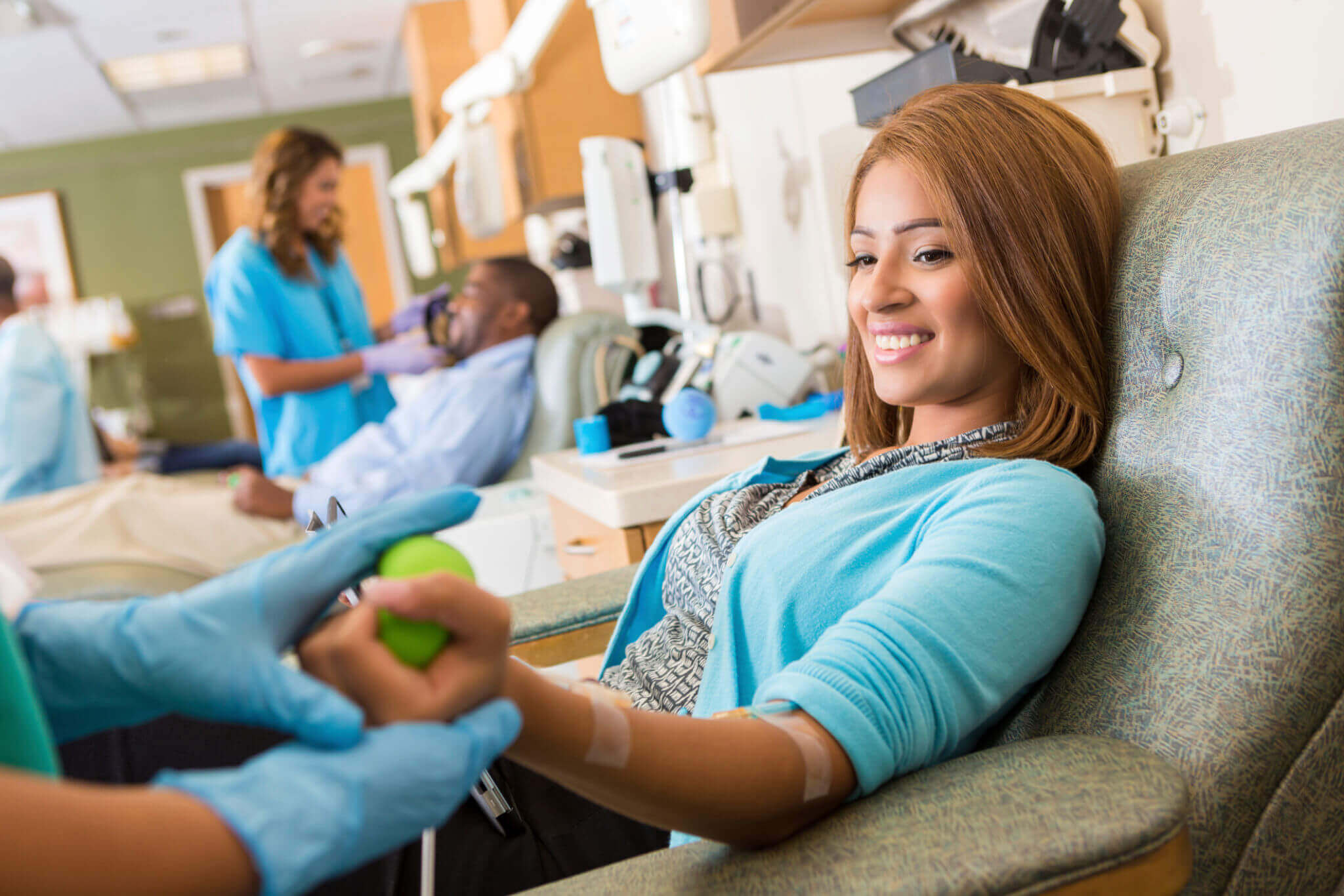A woman donates blood while smiling at a medical professional.