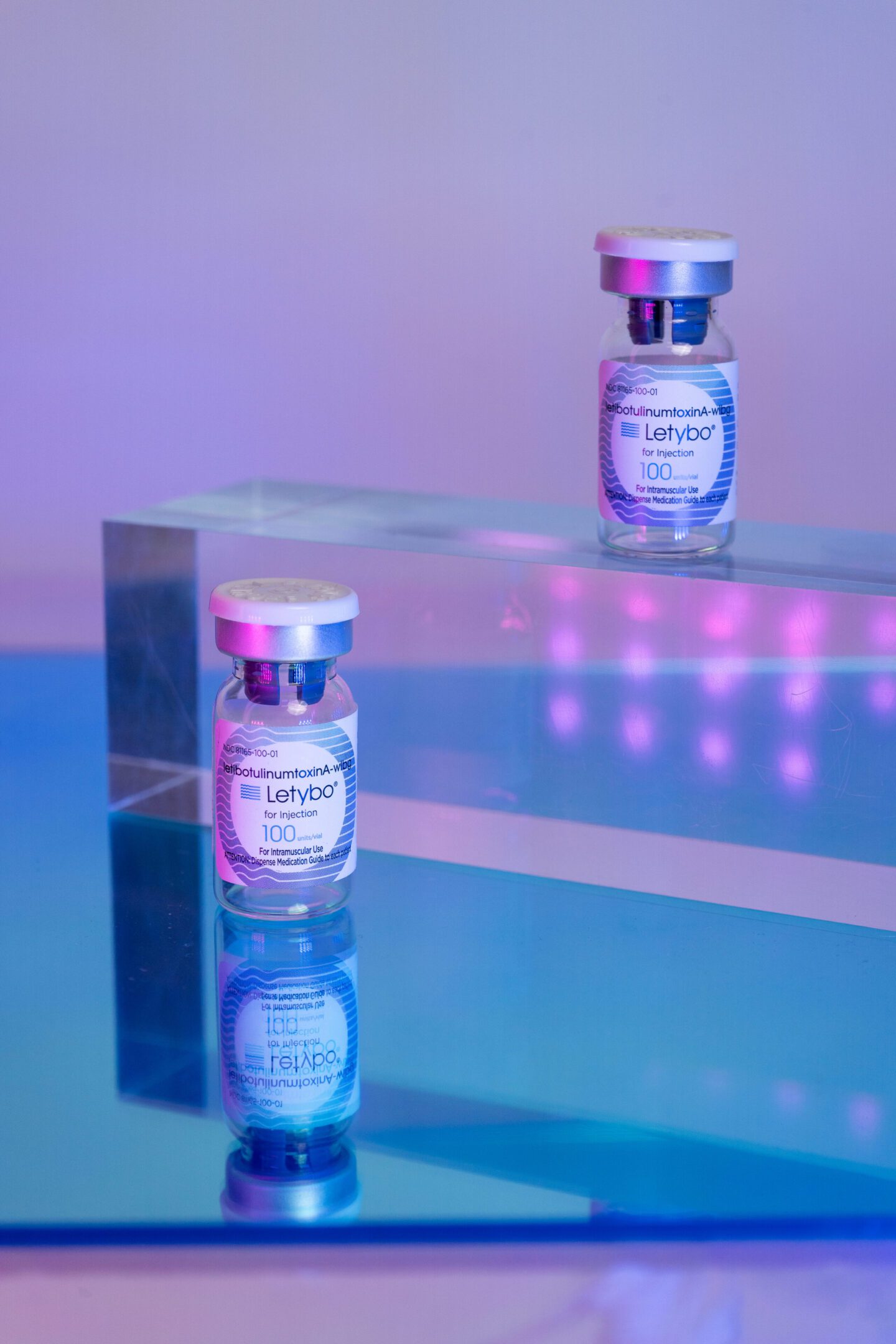 A bottle of perfume placed on a reflective surface with purple lighting.