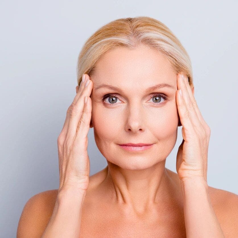 Mature woman gently touching her temples with a calm expression.