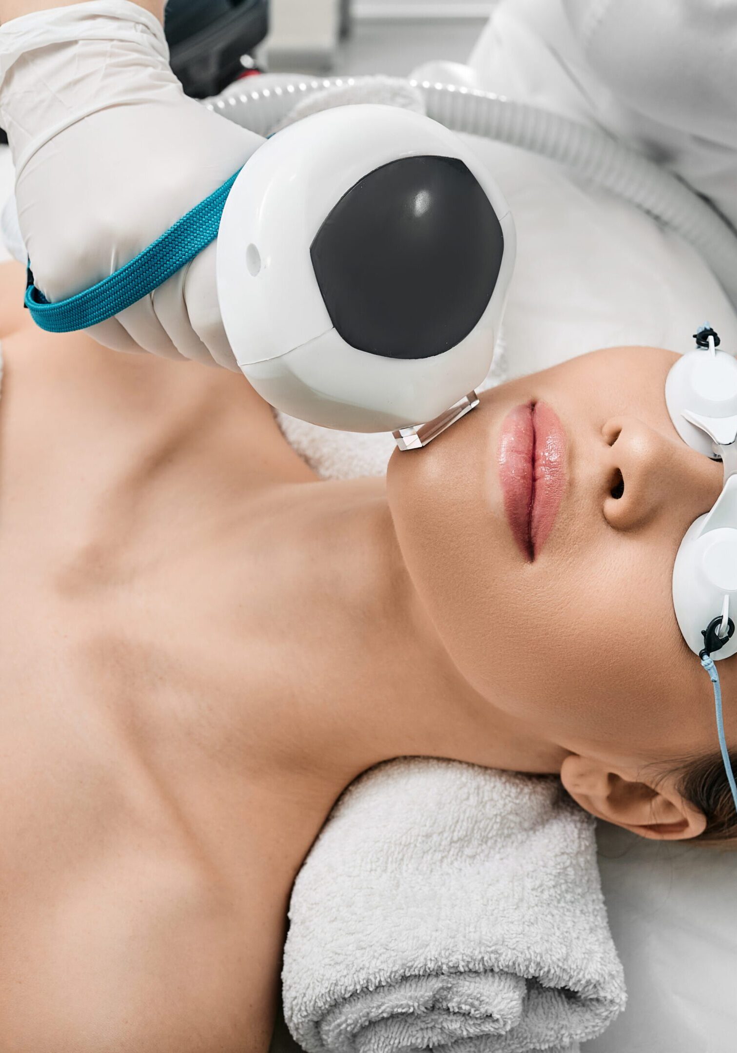 Woman receiving a facial treatment with cooling eye pads and a device.
