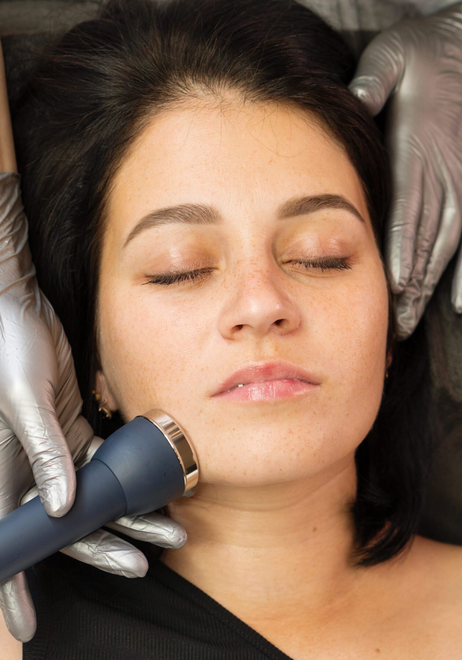 Woman receiving a facial treatment with a handheld device.