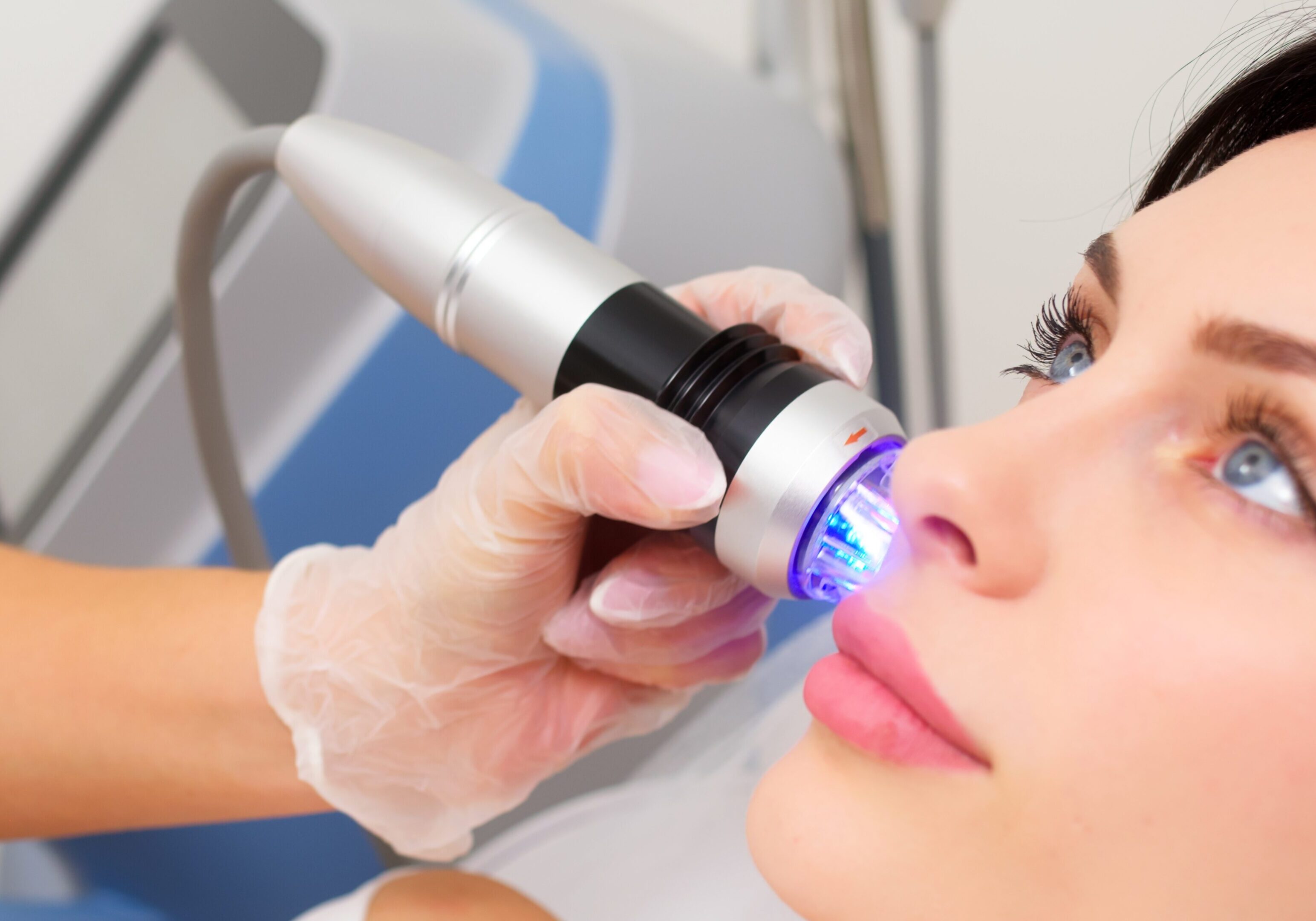 Close-up of a woman receiving a facial skin treatment with a blue light device.