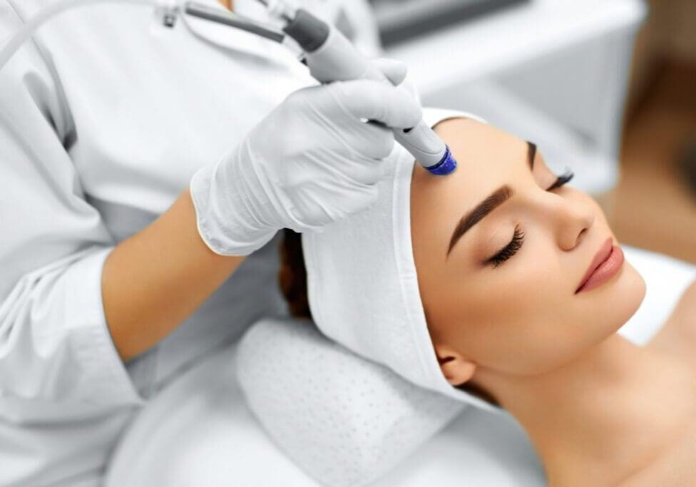 A woman receiving a facial treatment with a modern skincare device.