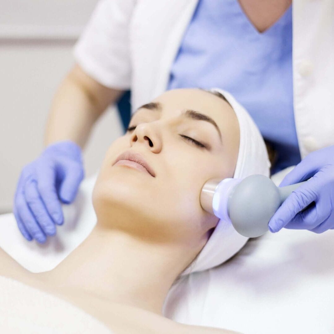 Woman receiving facial treatment with a handheld device at a spa.