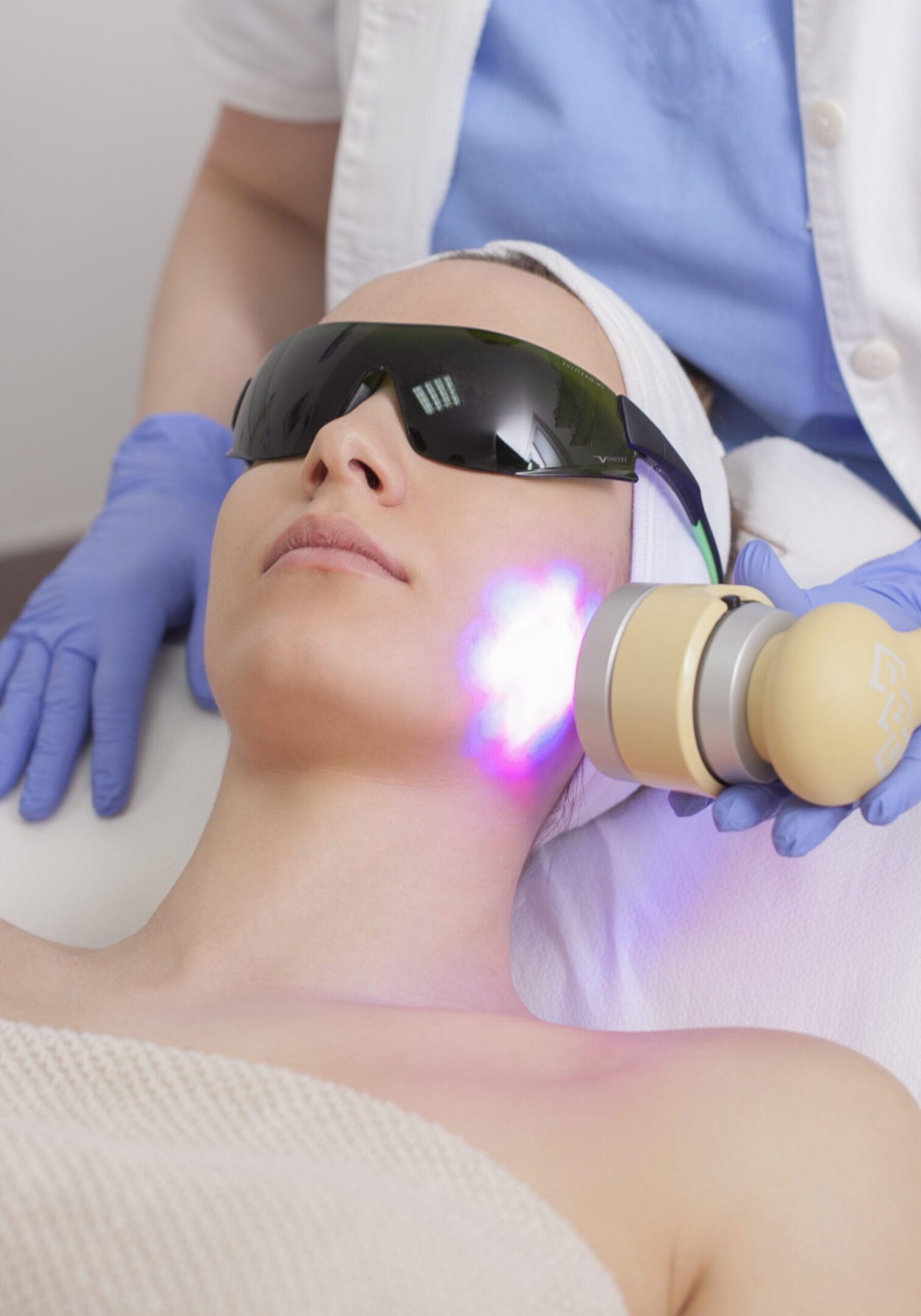 Woman receiving LED light therapy facial treatment at a spa.